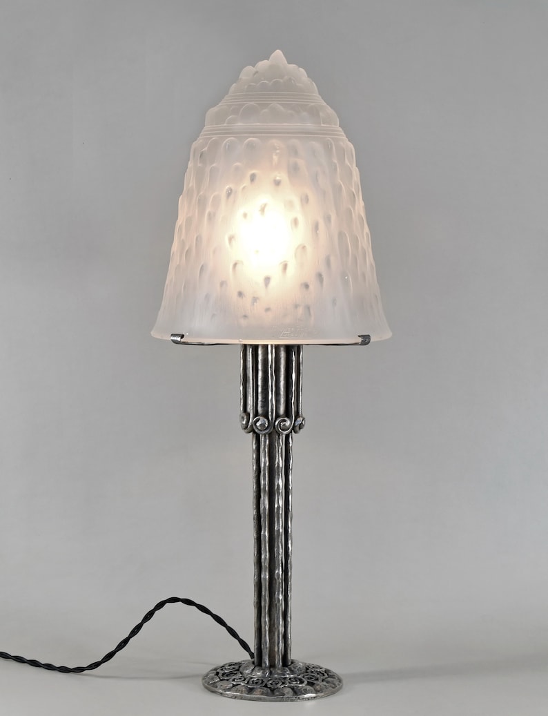May include: A silver table lamp with a frosted glass shade. The shade has a textured, bumpy surface. The lamp base is made of metal and has a cylindrical shape with decorative details.
