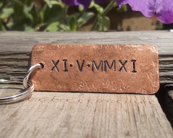May include: A copper keychain with a silver key ring. The copper tag has the Roman numeral date "XI-V-MMXXI" engraved on it.