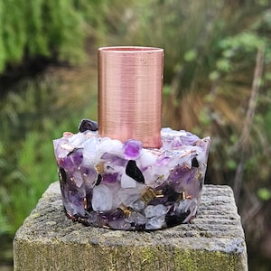 May include: A copper candle holder with a base made of amethyst, clear quartz, and black stones. The holder is sitting on a wooden surface.