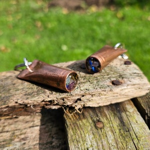 May include: Two copper keyrings with a clear cylinder filled with colourful glass beads. The keyrings are on a weathered wooden surface.