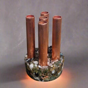 May include: A copper pipe vase with a base made of green, brown, and clear crystals. The vase has five openings for flowers.