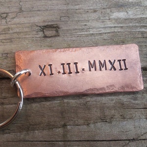 May include: A copper keyring with a silver ring. The keyring has the Roman numerals "XI.III.MMXII" engraved on it.
