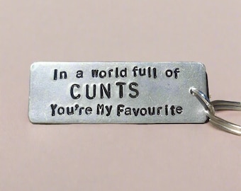 May include: A silver metal keychain with the text "In a world full of CUNTS You're My Favourite".