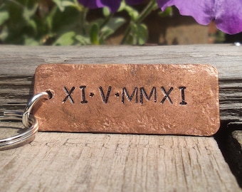 May include: A copper keychain with a rectangular tag engraved with the Roman numeral date "XI.V.MMXI".