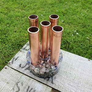 May include: A copper pipe pen holder with a round base filled with colorful stones and crystals.