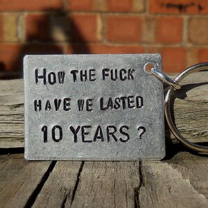 May include: A silver metal keychain with a tag that reads "How the fuck have we lasted 10 years?"