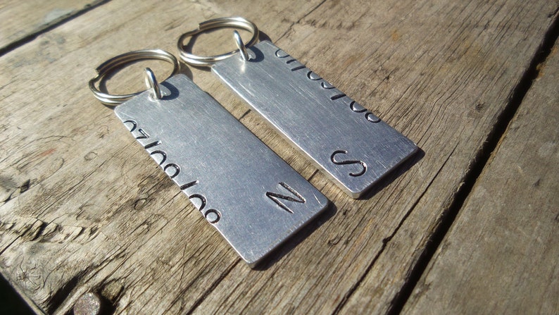 Puede incluir: Dos llaveros de plata con texto grabado. Un llavero dice "Te amo" y el otro dice "S" con un coraz&oacute;n.