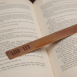 Könnte beinhalten: Eine weiße Keramik-Tasse mit schwarzem Henkel und dem Text "But First, Coffee" in schwarzer, handschriftlicher Schrift. Die Tasse steht auf einer weißen Oberfläche.