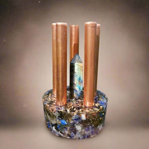 May include: A unique decorative piece featuring copper rods surrounding a central crystal. The base is a mix of blue, green, and gold materials. The crystal has blue and gold hues.