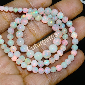 May include: A strand of white opal beads with iridescent rainbow flashes. The beads are round and smooth, and they are strung on a clear thread. The beads are approximately 6mm in diameter.