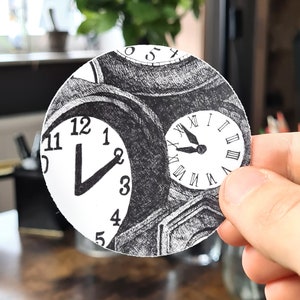 Könnte beinhalten: Eine Schwarzweißzeichnung eines Zifferblatts mit römischen Ziffern und eines Zifferblatts mit arabischen Ziffern. Die Zeichnung befindet sich auf einem runden Stück Papier.