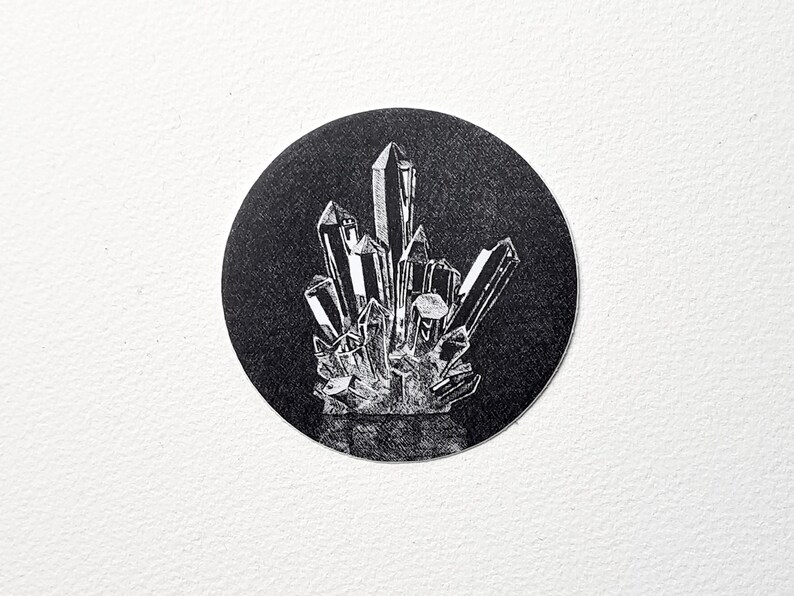 May include: A black and white illustration of a cluster of crystals. The crystals are depicted with sharp, angular facets and are arranged in a dense, upright formation within a black circular background. The image is set against a white backdrop.