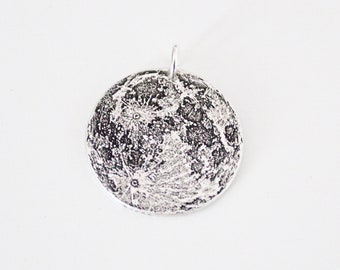 May include: A silver pendant shaped like the moon with a detailed surface texture.
