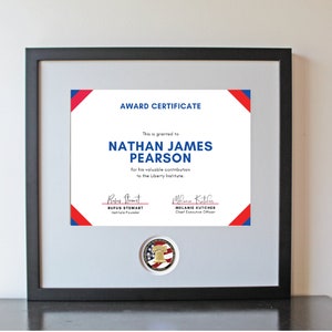 May include: Framed award certificate with a black frame and a gray mat. The certificate has a white background with blue and red accents. The text reads "AWARD CERTIFICATE" and names Nathan James Pearson.