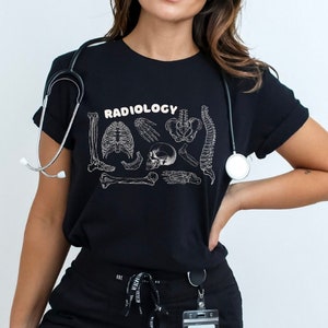 Op de afbeelding: Een zwart T-shirt met het woord "RADIOLOGY" in wit gedrukt op de voorkant. Het shirt heeft een afbeelding van verschillende botten en een schedel.