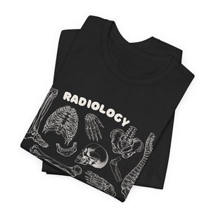 Op de afbeelding: Zwart T-shirt met een witte print van verschillende botten en het woord "RADIOLOGY" in een wit bubbelschrift.