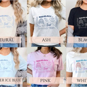 Op de afbeelding: Zes verschillende t-shirts in de kleuren naturel, as, zwart, heide-ijsblauw, roze en wit met het woord "RADIOLOGY" en een afbeelding van anatomische botten en een schedel op de voorkant.
