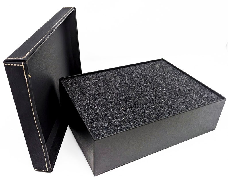 May include: An open black gift box with a textured, dark gray interior and a separate lid. The lid is black with white stitching around the edges. The box is on a white background.