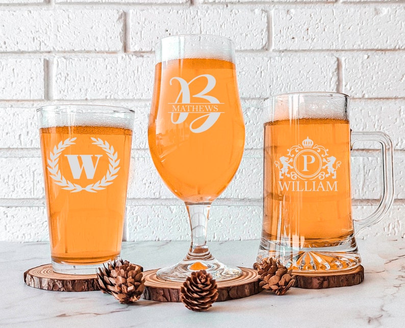 Pode incluir: Tr&ecirc;s copos de cerveja personalizados com designs diferentes. O primeiro copo tem uma coroa de louro com a letra W dentro. O segundo copo tem a letra B com o nome Mathews abaixo. O terceiro copo tem uma coroa com a letra P dentro e o nome William abaixo.