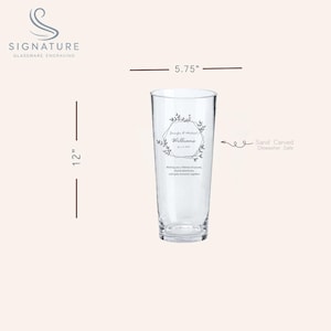 Puede incluir: Un vaso alto y transparente con un grabado personalizado. El vaso mide 30,48 cm de alto y 14,61 cm de ancho. El grabado incluye nombres, una fecha y un dise&ntilde;o floral. El texto dice: "Dese&aacute;ndoles una vida de amor, aventuras compartidas y momentos tranquilos juntos."
