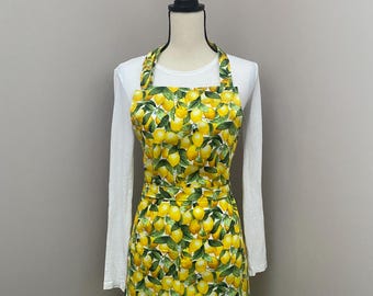 May include: A yellow and green apron with a lemon print. The apron has adjustable straps and a large pocket in the front.