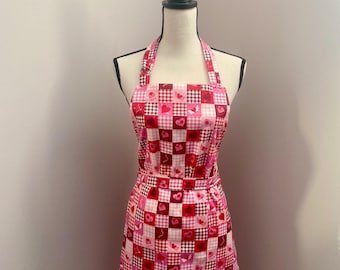 May include: A pink and red checkered apron with a heart pattern. The apron has a halter neck strap and a tie at the waist.