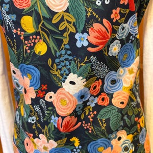 Peut inclure: Un tablier bleu marine orn&eacute; d'un motif floral vibrant. Le design pr&eacute;sente un assortiment de fleurs color&eacute;es dans des tons de rose, de bleu et de corail, avec des feuilles vertes et des fruits jaunes. Le tablier est en tissu r&eacute;sistant.