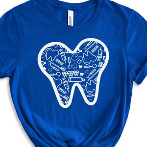 May include: A royal blue t-shirt with a white outline of a tooth. The tooth is filled with a pattern of dental tools and other dental-related imagery.