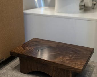 May include: A rectangular wooden stool with a dark brown finish and visible wood grain patterns. The stool features a flat top surface and two side supports with arched cutouts at the base. The text StreamStool™ and a circular logo are visible.