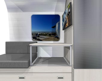 May include: Interior view of a modern RV with a gray sofa, a small desk, and a window with a view of the beach. A flat-screen TV is mounted on the wall. The cabinetry is light wood with a minimalist design.