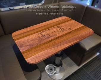 May include: A wooden table top with a laser engraved design of an Airstream trailer. The table top is made of walnut wood and has a natural finish. The text "CraeftStream Dinette Tabletops" and "Handmade Works for Your Airstream Travel Trailer" is visible on the table top.