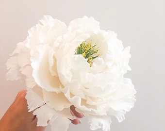 May include: A large, white, artificial peony flower with a yellow center. The flower is made of fabric or paper and has a realistic appearance.