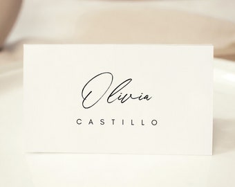 May include: White place card with black calligraphy text. The text reads "Olivia Castillo".