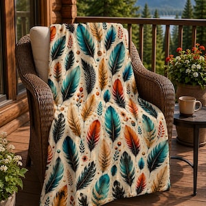 May include: A soft throw blanket featuring a repeating pattern of feathers in shades of teal, orange, and gold against a cream background. The design includes small sprigs of berries and dots interspersed among the detailed feather illustrations.