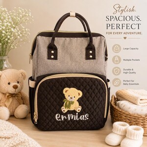 May include: A gray and brown diaper bag with a teddy bear embroidery and the name "Ermias". The bag has multiple pockets and a large capacity. The text on the bag says "Stylish. Spacious. Perfect. For every adventure."