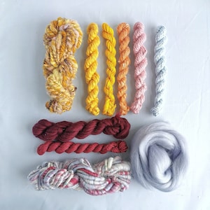 May include: Assortment of colorful yarn skeins and a ball of gray wool fiber. The yarn skeins are in shades of yellow, orange, pink, and light blue. The wool fiber is a light gray color.