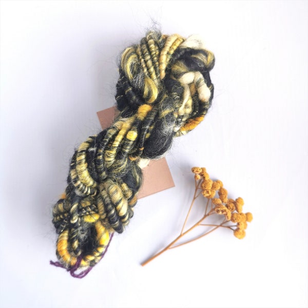 Black yellow handspun core art yarn for weaving, textile, and fiber crafts with yarn scraps.