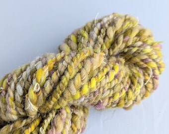 May include: A skein of chunky yarn in shades of yellow, green, brown, and pink. The yarn is hand-spun and has a rustic, textured look.
