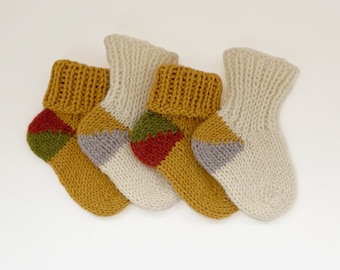 May include: Four pairs of knitted baby socks in white and yellow with colorful geometric patterns. The socks are made of soft yarn and are perfect for keeping little feet warm.