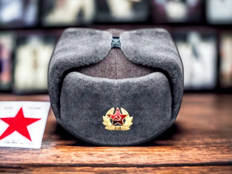 Może przedstawiać: Szary futrzaną czapka uszanka z czerwoną gwiazdą i złotym emblematem z przodu.