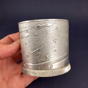 Peut inclure: Une tasse en m&eacute;tal argent&eacute; avec un motif d'&eacute;toiles et de com&egrave;tes. La tasse a une surface textur&eacute;e et une base c&ocirc;tel&eacute;e.