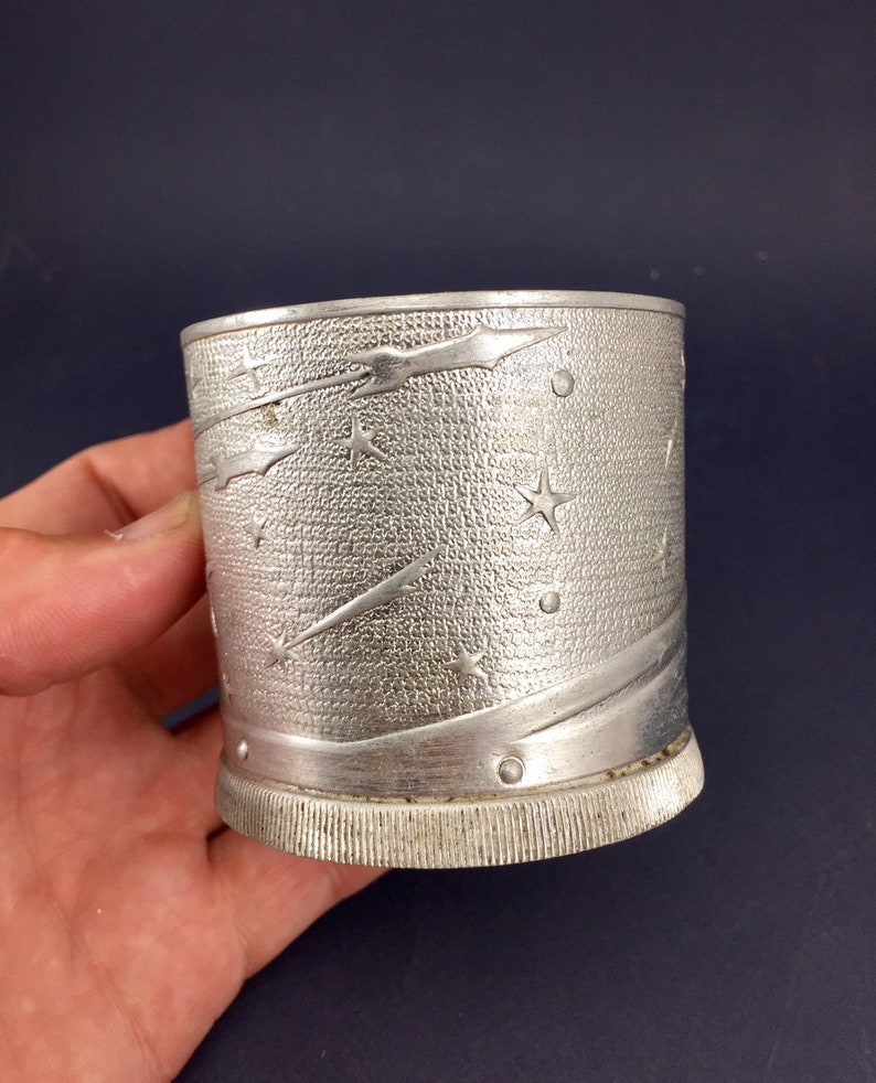 Peut inclure: Une tasse en m&eacute;tal argent&eacute; avec un motif d'&eacute;toiles et de com&egrave;tes. La tasse a une surface textur&eacute;e et une base c&ocirc;tel&eacute;e.