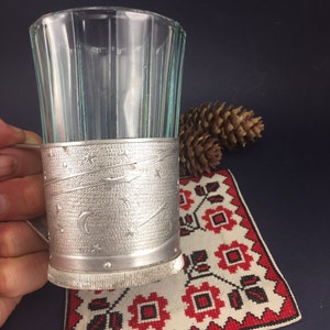 Peut inclure: Un porte-verre en argent avec un motif d&eacute;coratif d'&eacute;toiles et d'un croissant de lune. Le porte-verre est en m&eacute;tal et a une surface textur&eacute;e. Le porte-verre est pos&eacute; sur un tissu brod&eacute; rouge et blanc.