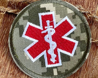 May include: A red and white embroidered medical symbol patch on a camouflage fabric background. The symbol is a star of life with a snake and staff in the center.
