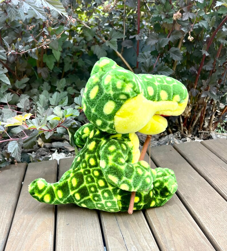 May include: Green and yellow plush crocodile toy holding a brown stick. The crocodile has a patterned design on its body.