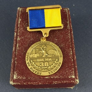 May include: A gold medal with a blue and yellow ribbon. The medal features a depiction of a nuclear power plant and the text "Ликвидация Наследствий Аварии На ЧАЭС 1986-2016 30 Років" (Liquidation of the Consequences of the Chernobyl Accident 1986-2016 30 Years).