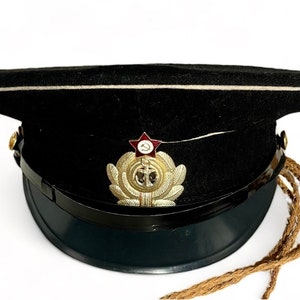 May include: A black military style hat with a gold anchor and red star insignia. The hat has a white band and a brown cord.