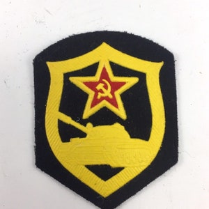 Może przedstawiać: Naszywka haftowana w kolorze czarnym i żółtym z czerwoną gwiazdą i sylwetką czołgu. Gwiazda zawiera sierp i młot.