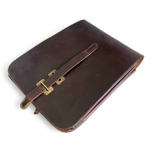 May include: A brown leather satchel with a brass buckle and strap closure. The bag has a worn, vintage look.