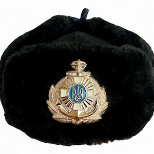 Può includere: Cappello ushanka in pelliccia nera con un emblema dorato e blu con un tridente e un'ancora.